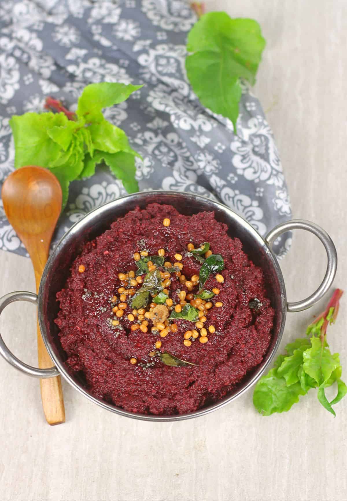 beetroot thogayal with a wooden spoon and beet leaves in the background