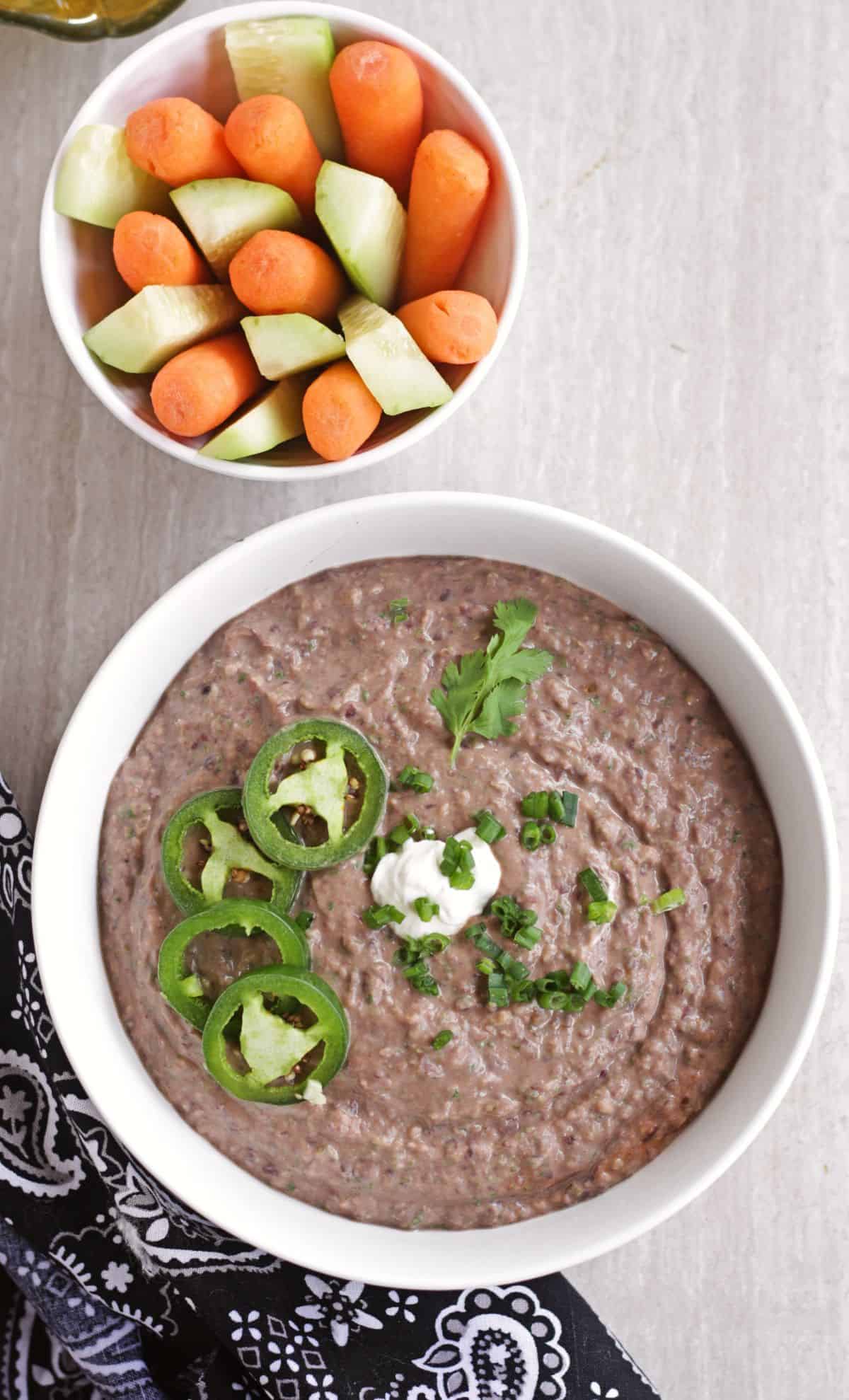 black bean dip in a bowl with slice jalapenos and sour cream and vegetables in the side