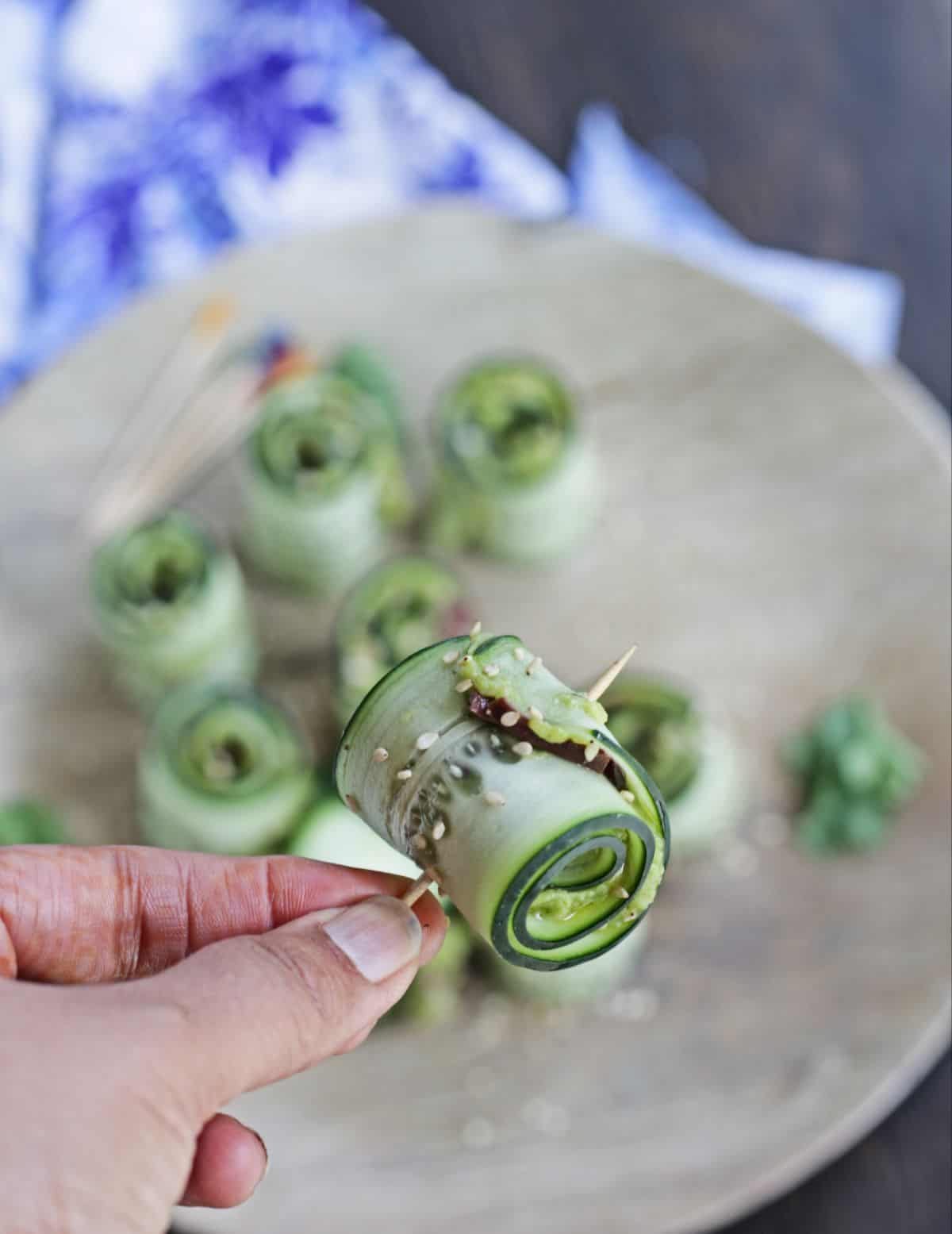 One single cucumber roll held in hand with a toothpick