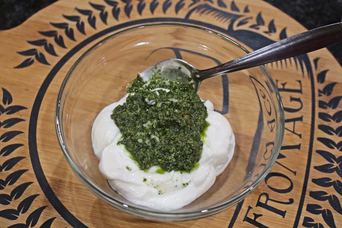 Pesto and mayo in a glass bowl with a spoon.