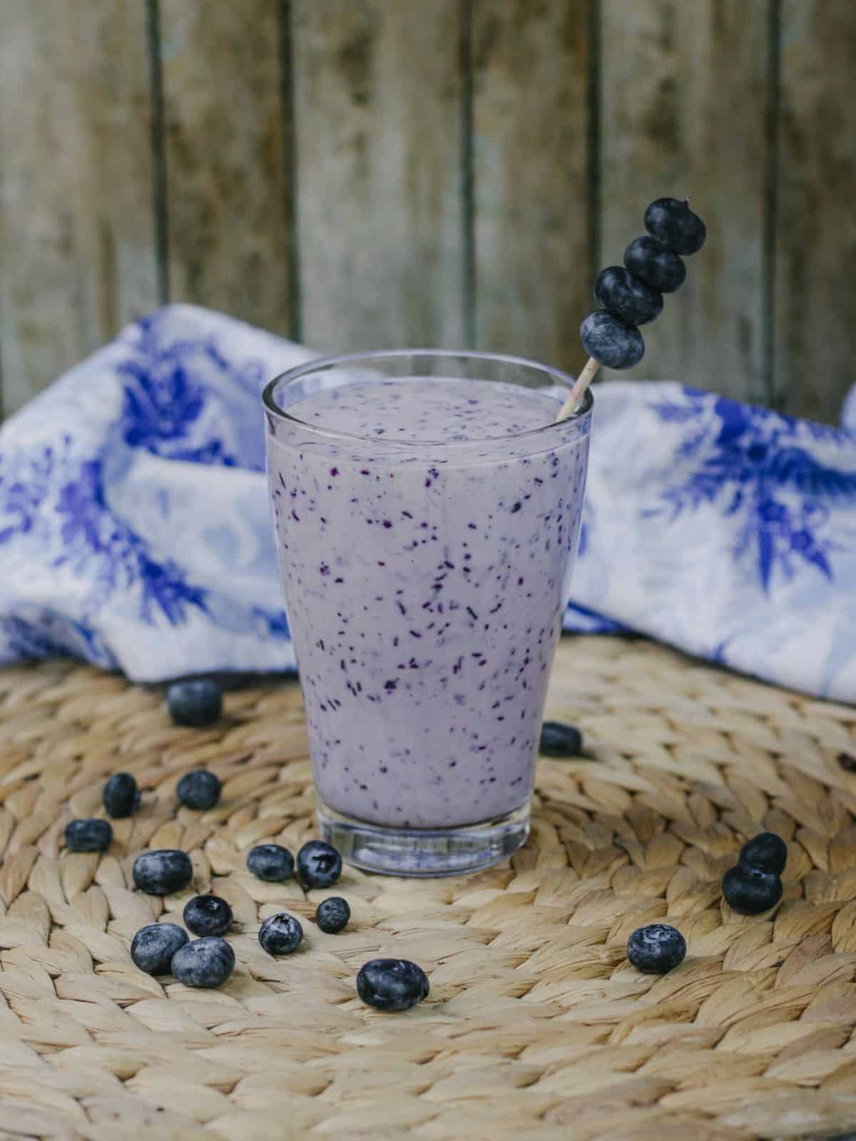 A tall glass of blueberry flavored lassi with blueberries on the side.