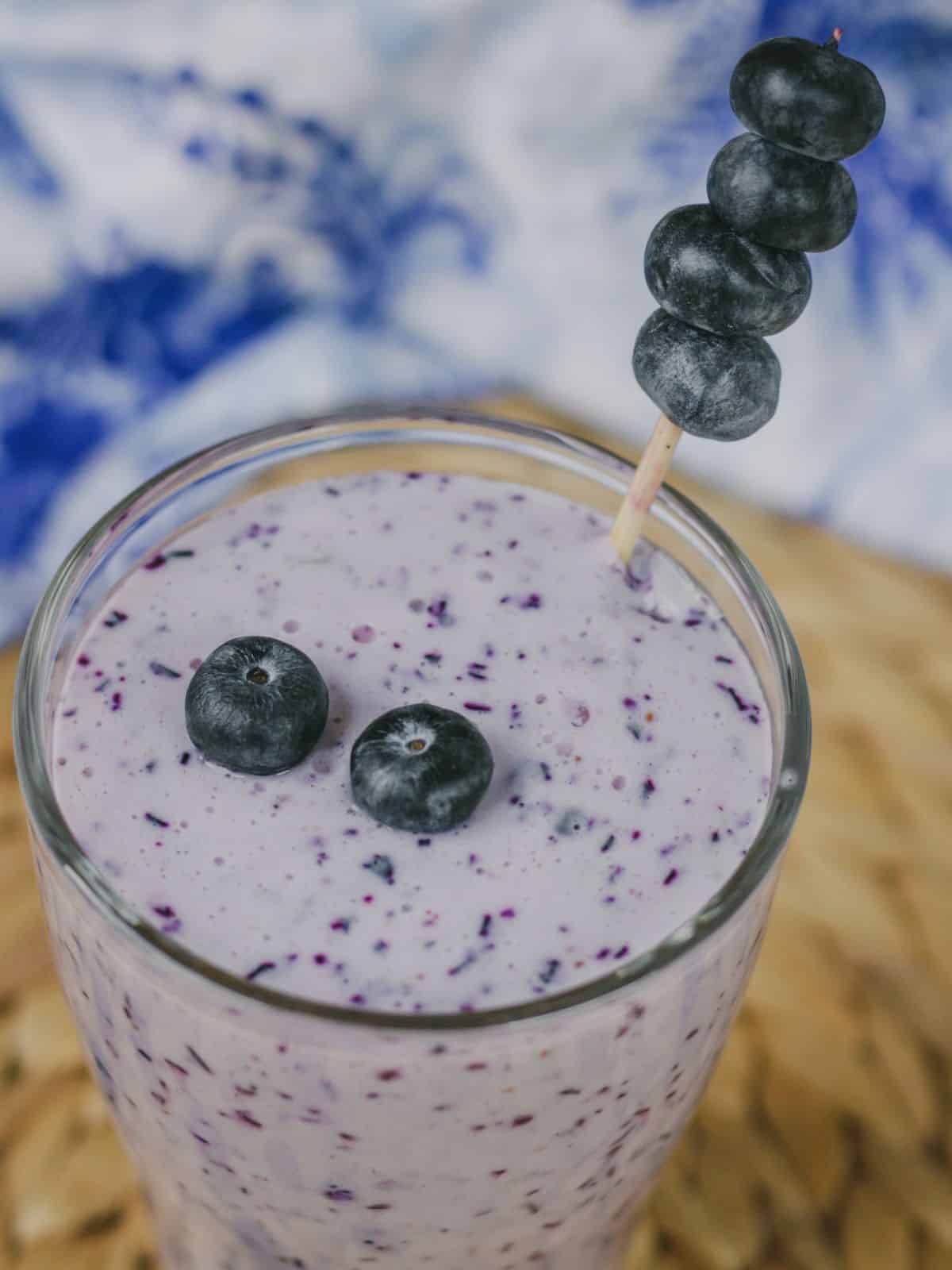 A glass of blue smoothie with blueberry as garnish.