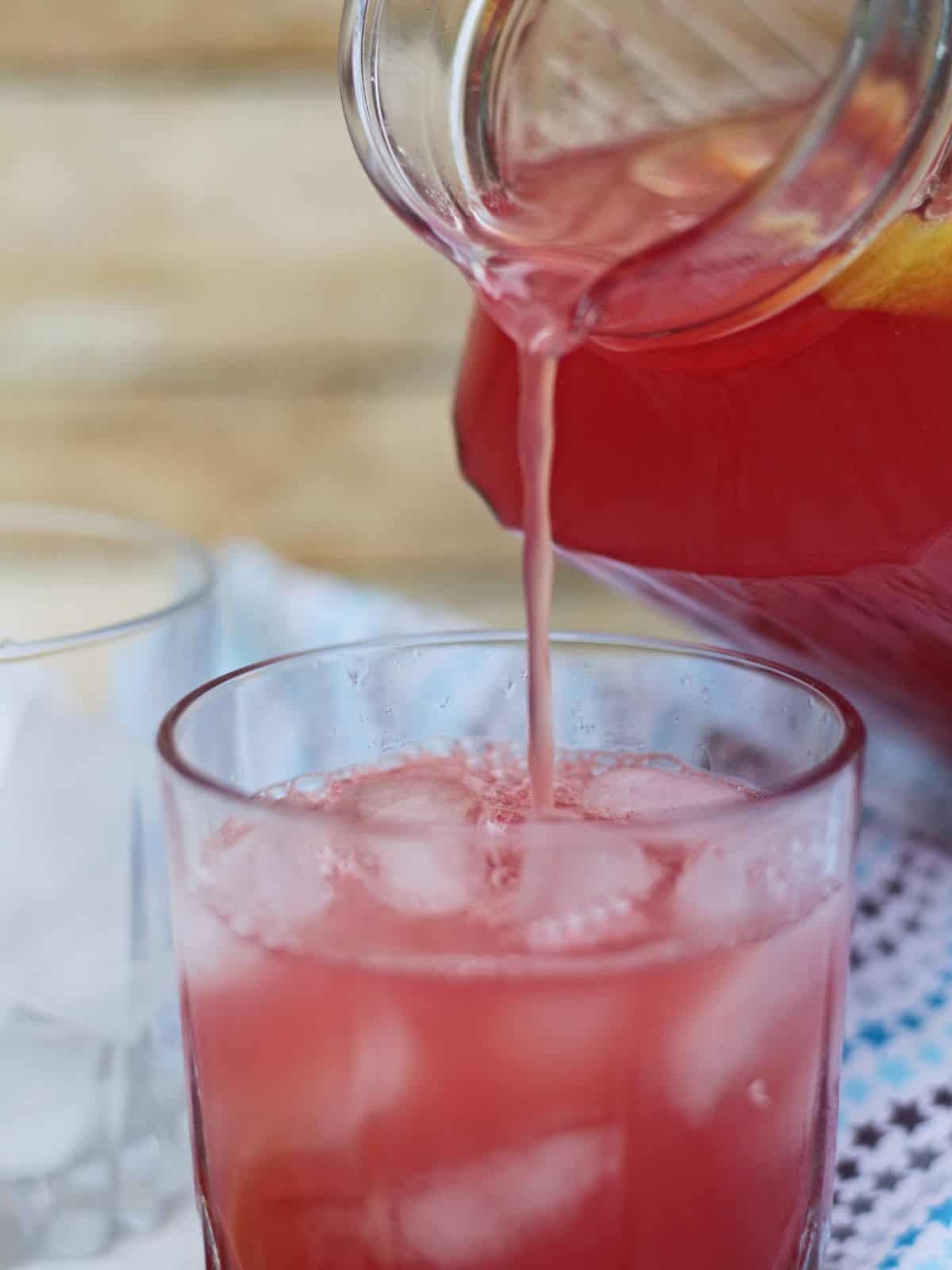 Pouring pink lemonade in a glass with ice.