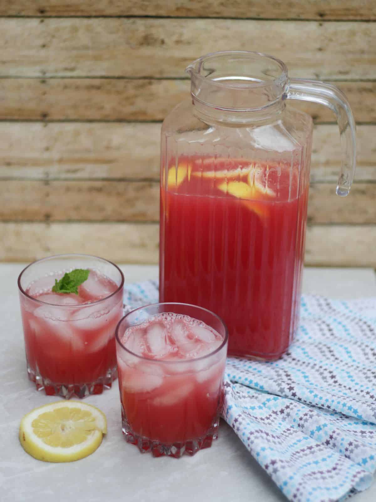A pitcher and two glasses of pink lemoande.