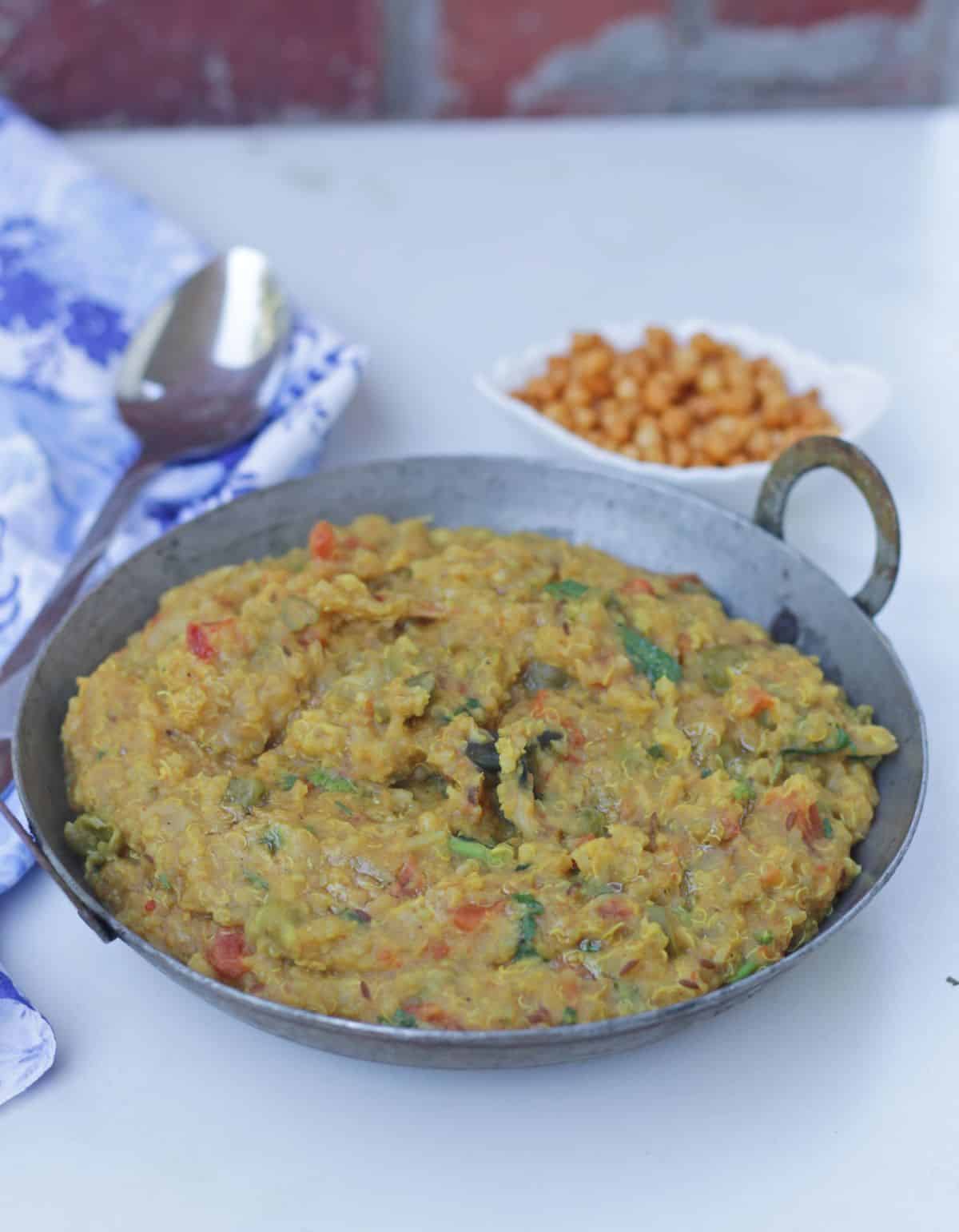 A bowl of moong dal and quinoa khichdi with a spoon and boondi on side.